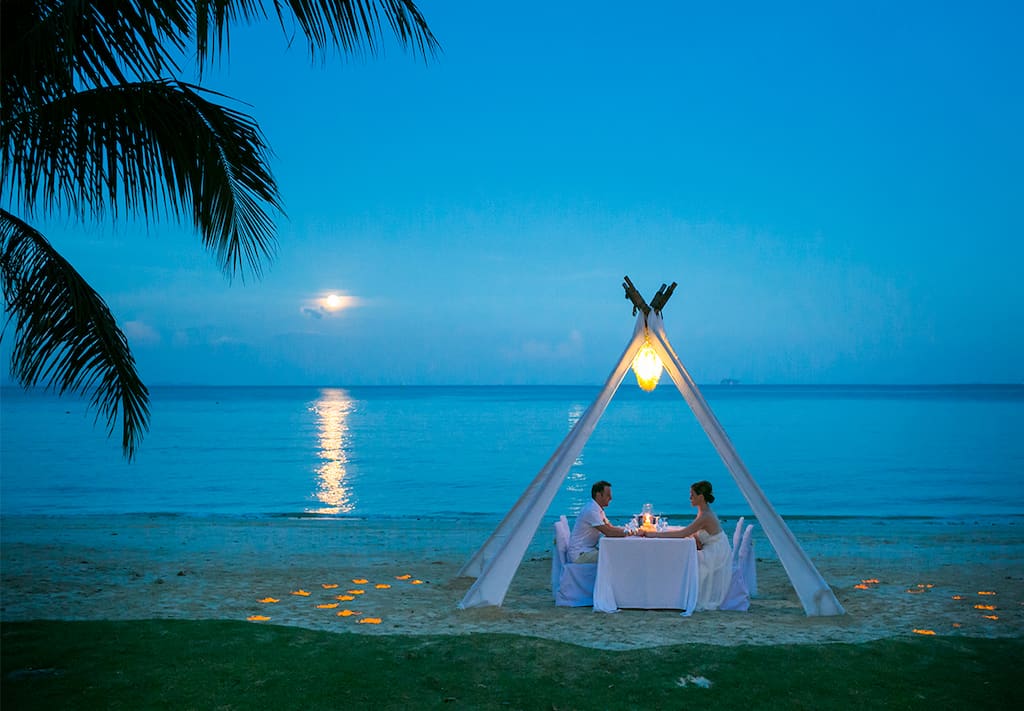 A couple having a romantic dinner on the beach in Thailand.